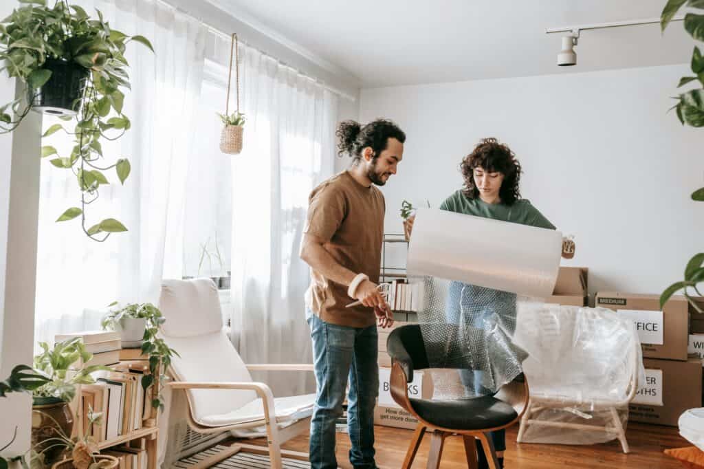 A couple is wrapping a chair with bubble wrap in the concept of saving money when relocating to Finchley.