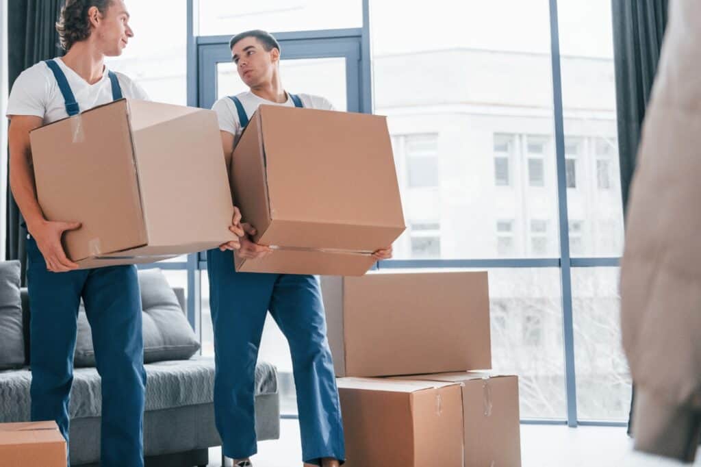 Two professional movers carrying cardboard from a modern flat during the moving day